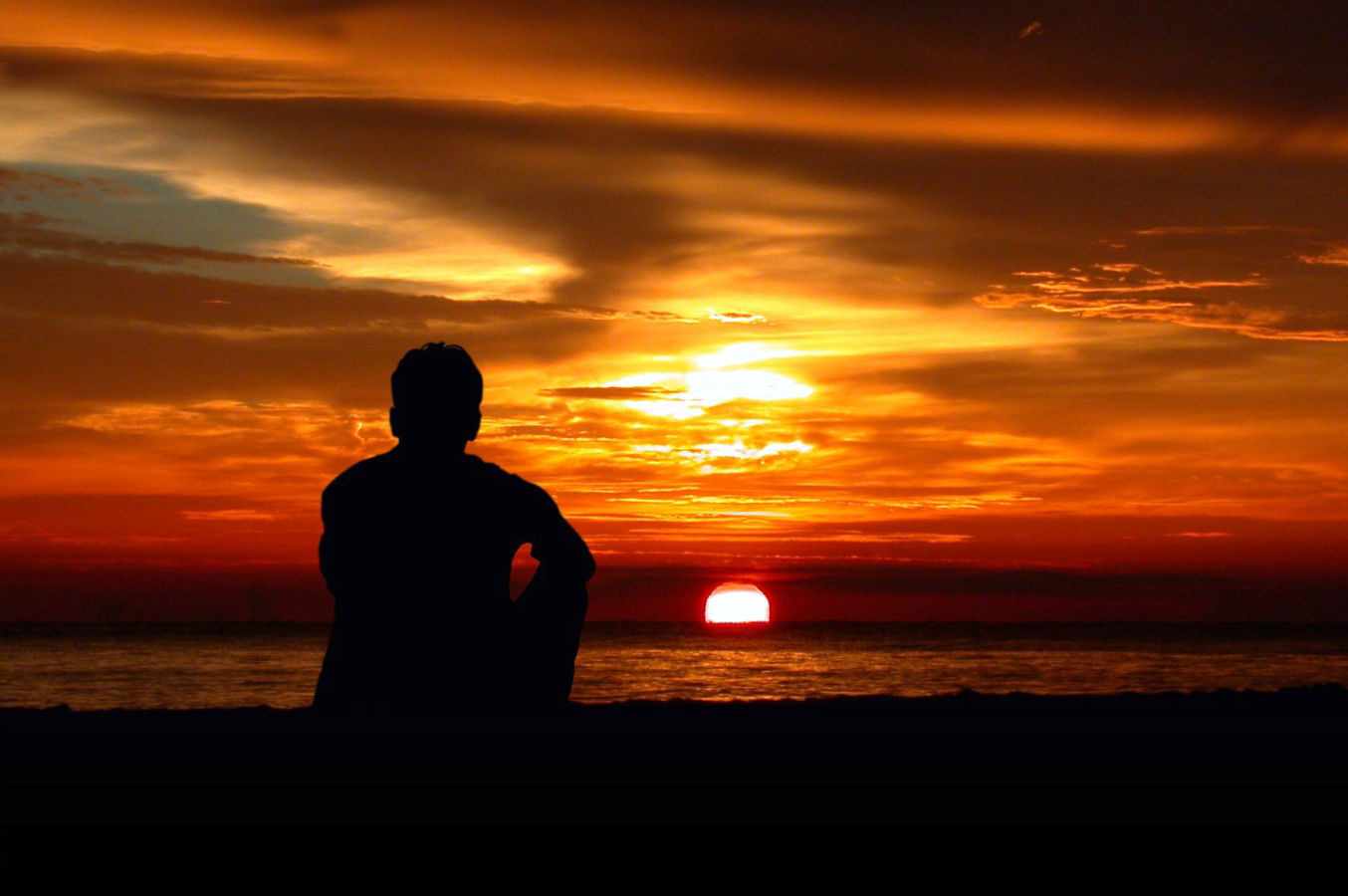 Un uomo seduto sulla spiagga al tramonto